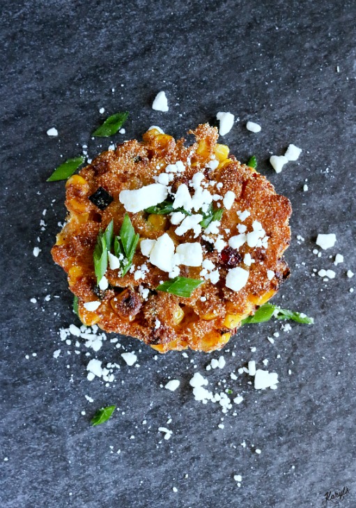 overhead shot of finished corn cakes on a black platter, garnished with cheese and spring onions