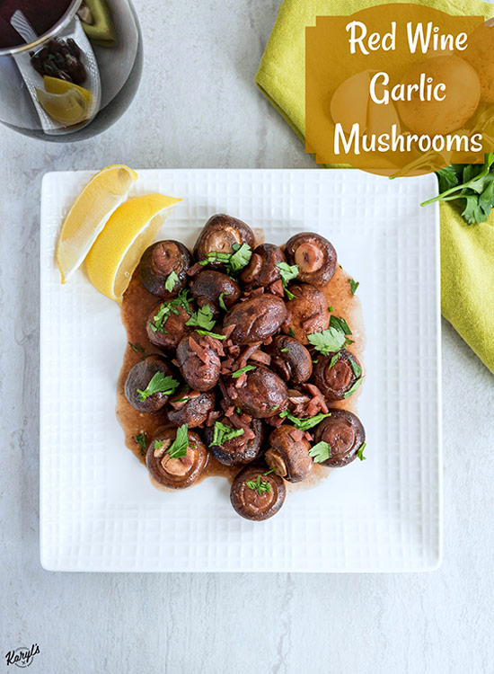 overhead shot of finished red wine garlic mushrooms on a white plate wiht a glass of wine plus a green napkin in the background