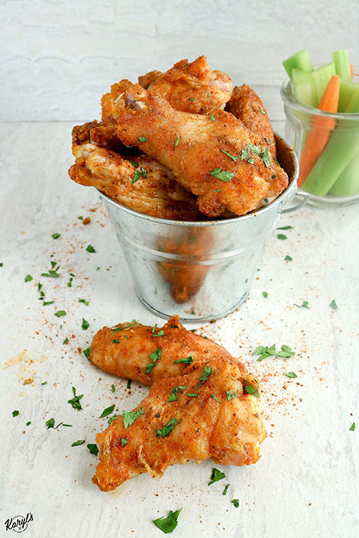 close up shot of chicken wings in a metal bucket, with carrots & celery in a clear jar on the side