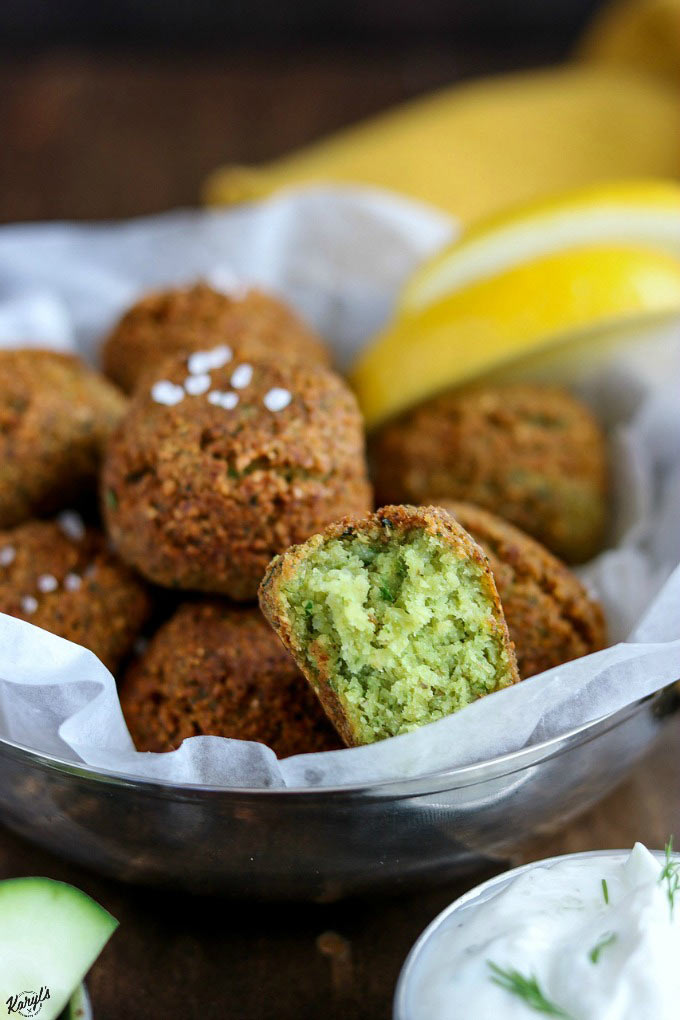 close up shot of finished Falafel in a metal bowl, with one piece of Falafel cut open to see the inside