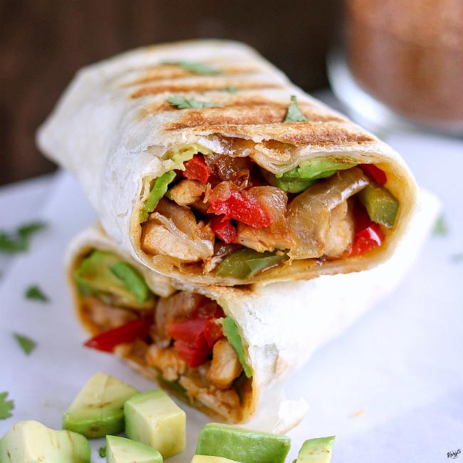 front shot of Crispy Chicken Fajita Wrap, cut in half, stacked on top of each other, with pieces of avocado