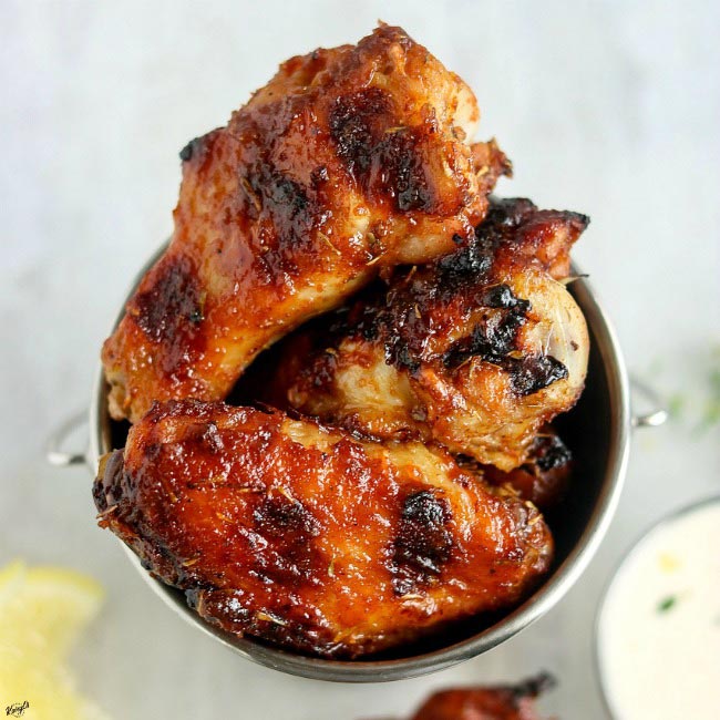overhead shot of Grilled Honey Bourbon Chicken Wings in small metal serving bucket, with dipping sauce to the side