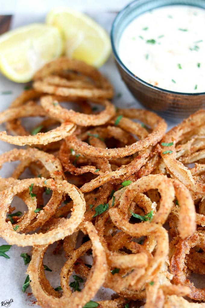 overhead shot of Crispy Fried Onion Straws on a piece of white parchment paper, with side of garlic aoili in top right corner