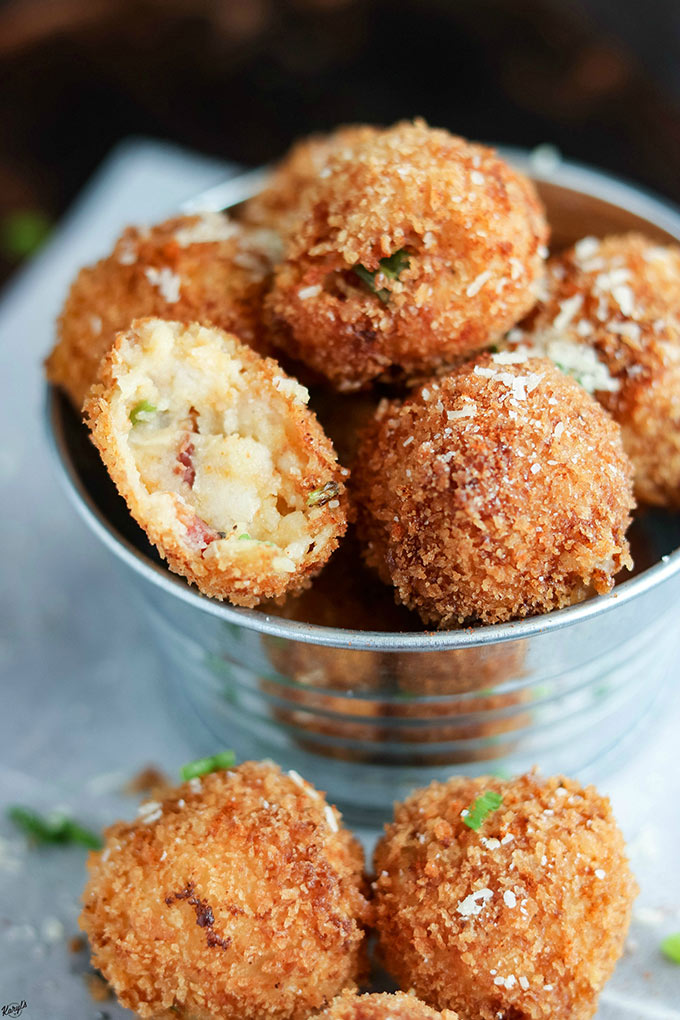 close up shot of finished mashed potato balls in a metal bucket, with a few balls on the parchment paper