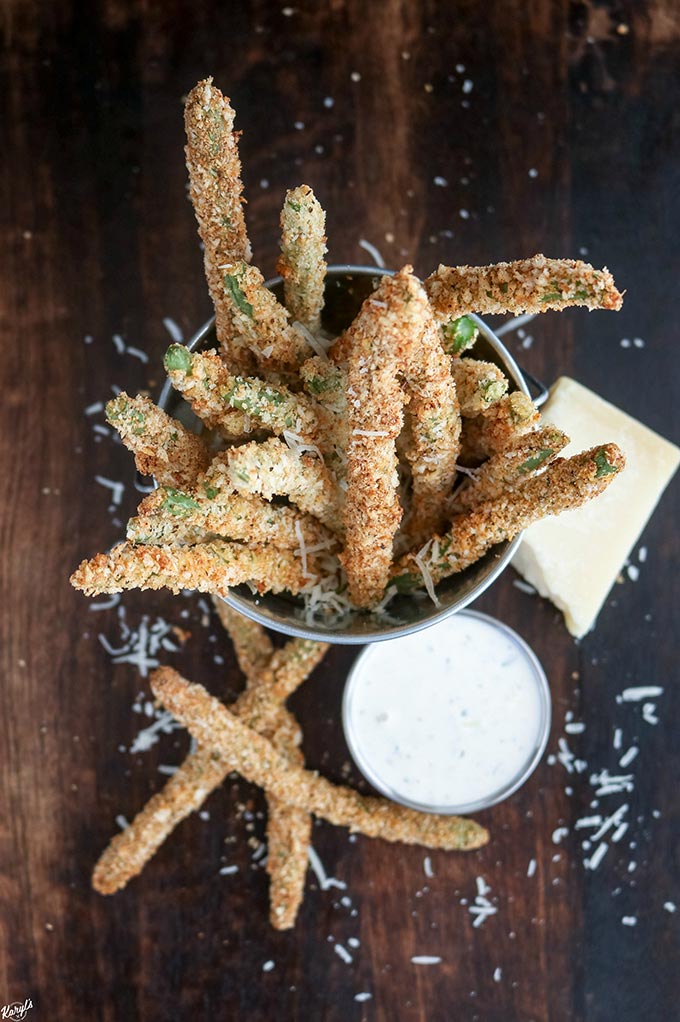 overhead shot of Baked Green Bean Fries in a metal bucket with a side of ranch in front and a block of Parmesan cheese on the side