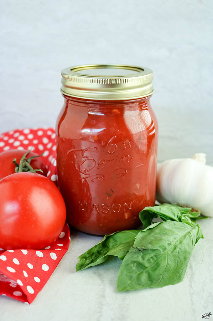 close up shot of marinara sauce in a jar, with fresh tomatoes, basil and garlic on the side