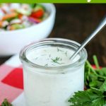 close up shot of finished ranch dressing in a glass jar with a spoon, with a salad in the background