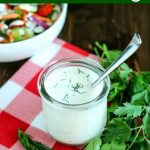 angled shot of finished ranch dressing in a glass jar with a spoon in the jar, with a salad in the background