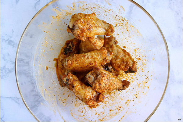 close up shot of wings tossed in sauce in a glass bowl