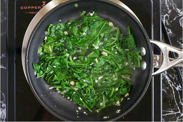 overhead process shot: wilted spinach with garlic and onions in a skillet