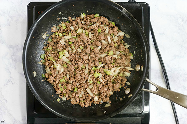 overhead process shot: venison, onion and celery cooked in a black skillet