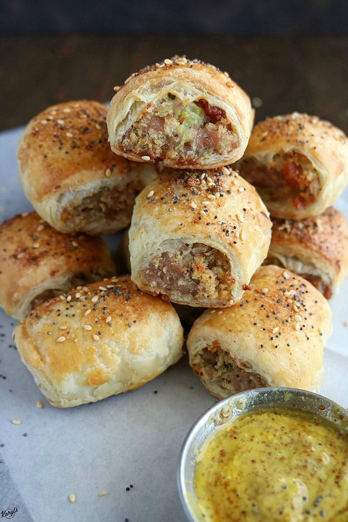 close up shot of finished sausage rolls in a pile on white paper. Side of mustard in a metal container in front