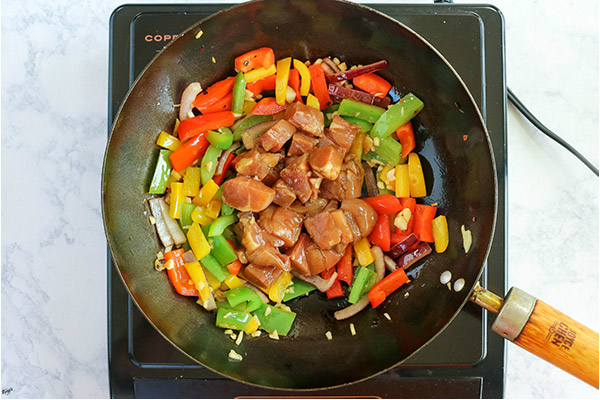 overhead process shot: drained chicken added to bell peppers and onions in a black wok
