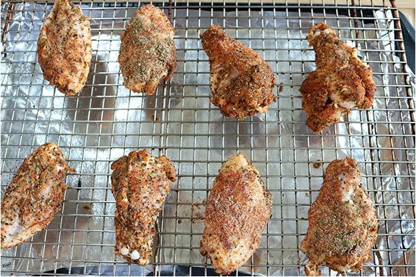 Process shot: close up shot of seasoned chicken wings on a baking sheet