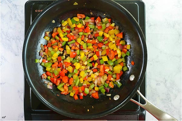 Overhead process shot: bell peppers, onion and garlic cooking in a black skillet