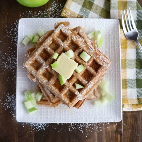 Overhead shot of a stack of finished Apple Cinnamon Waffles on a white plate, topped with diced apple