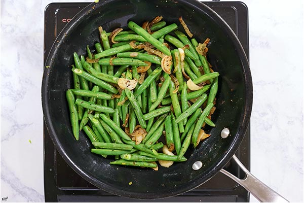 Overhead process shot: green beans, onion and garlic cooking in a black skillet