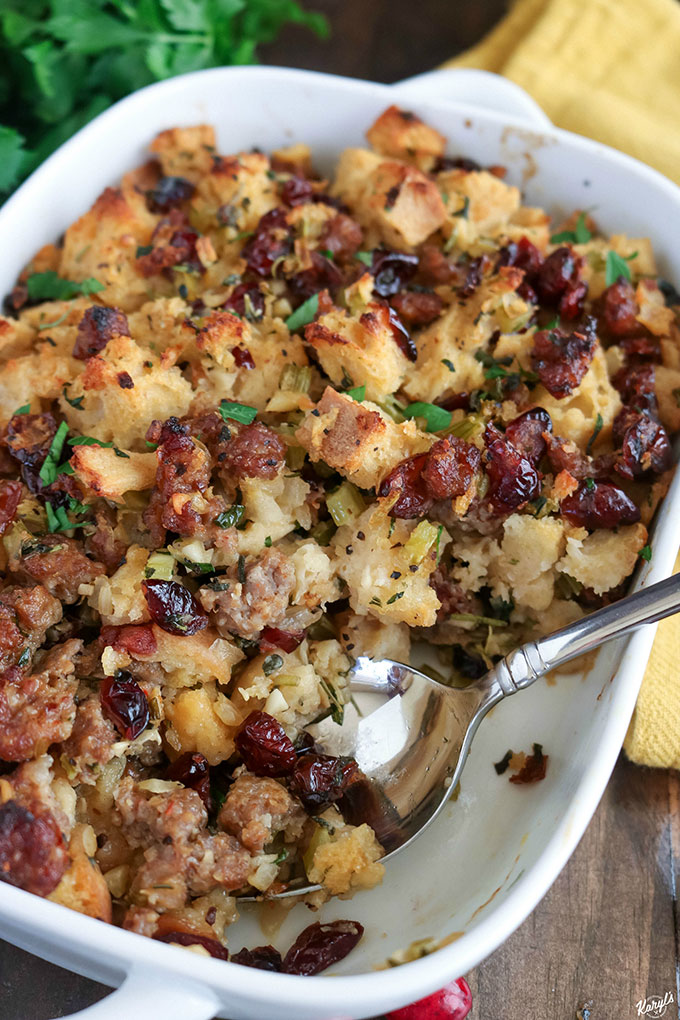Close up shot of finished Sausage Cranberry Sage Stuffing in a white baking dish with a spoonful of stuffing removed and a spoon in the baking dish